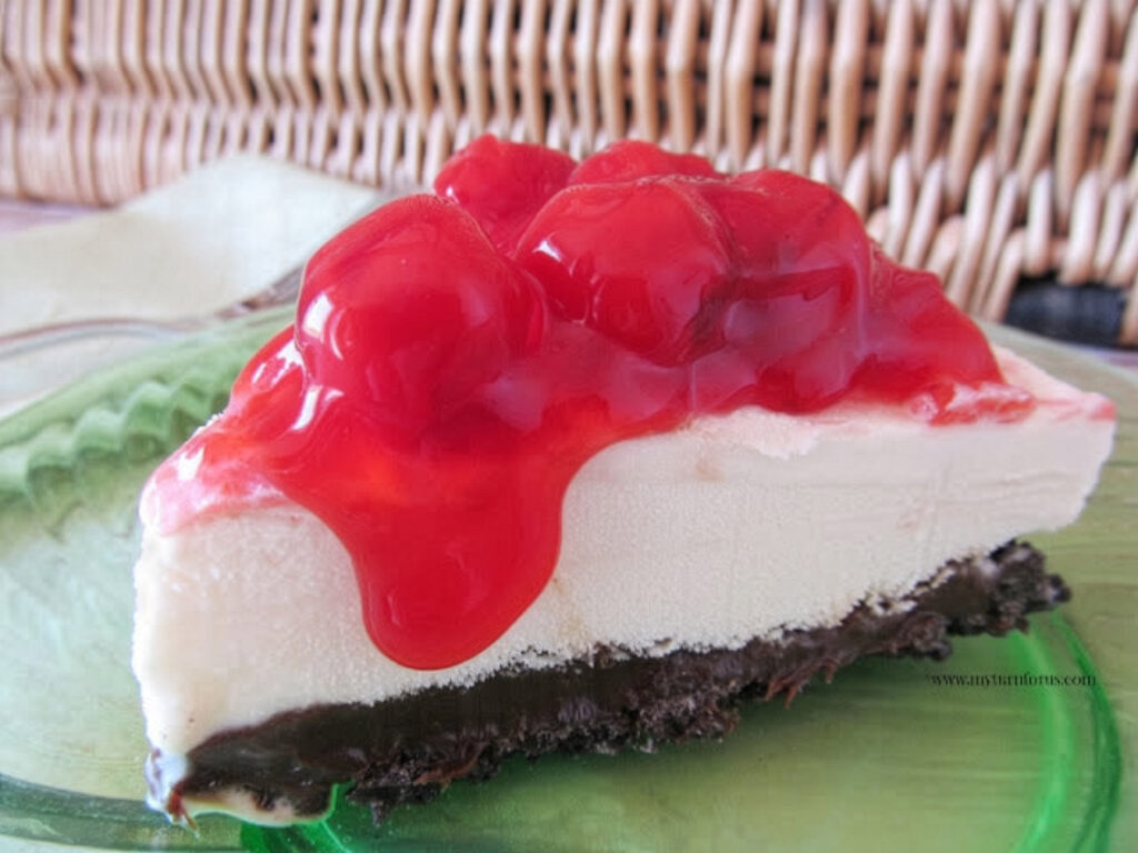 Slice of vanilla ice cream pie with Oreo crust, hot fudge layer, and cherry pie filling on top.