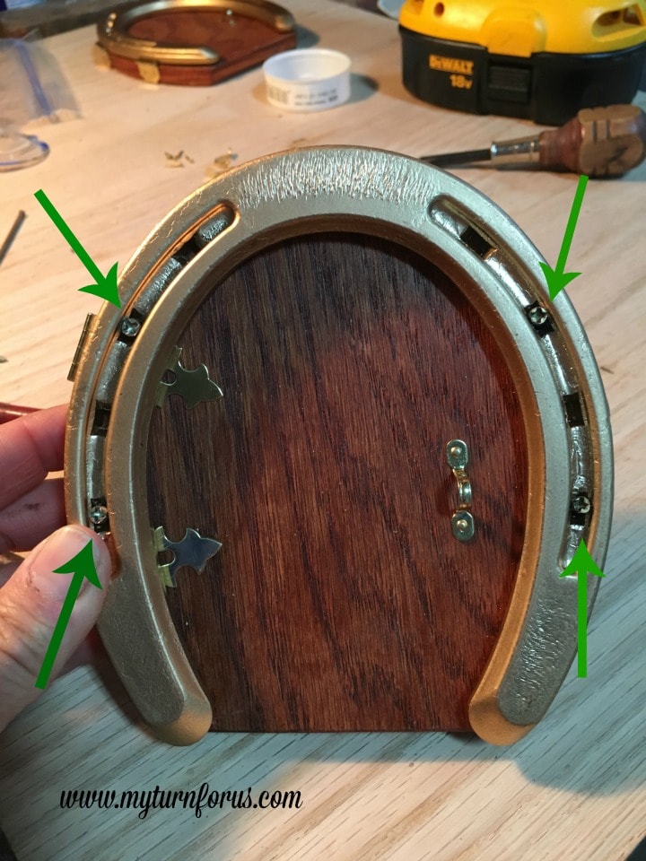 Horseshoe Fairy Door for the most magical fairy garden! https://www.myturnforus.com/2016/03/horseshoe-fairy-door.html Completed wooden fairy door framed with a gold horseshoe, with arrows showing the four screws that hold the horseshoe in place.