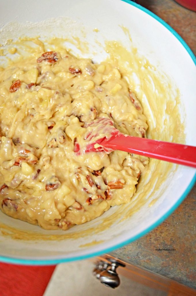Banana bread batter with chopped pecans being folded together with a red spatula.