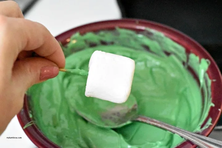 Dipping marshmallow into green melted candy for Leprechaun Hat Cookies
