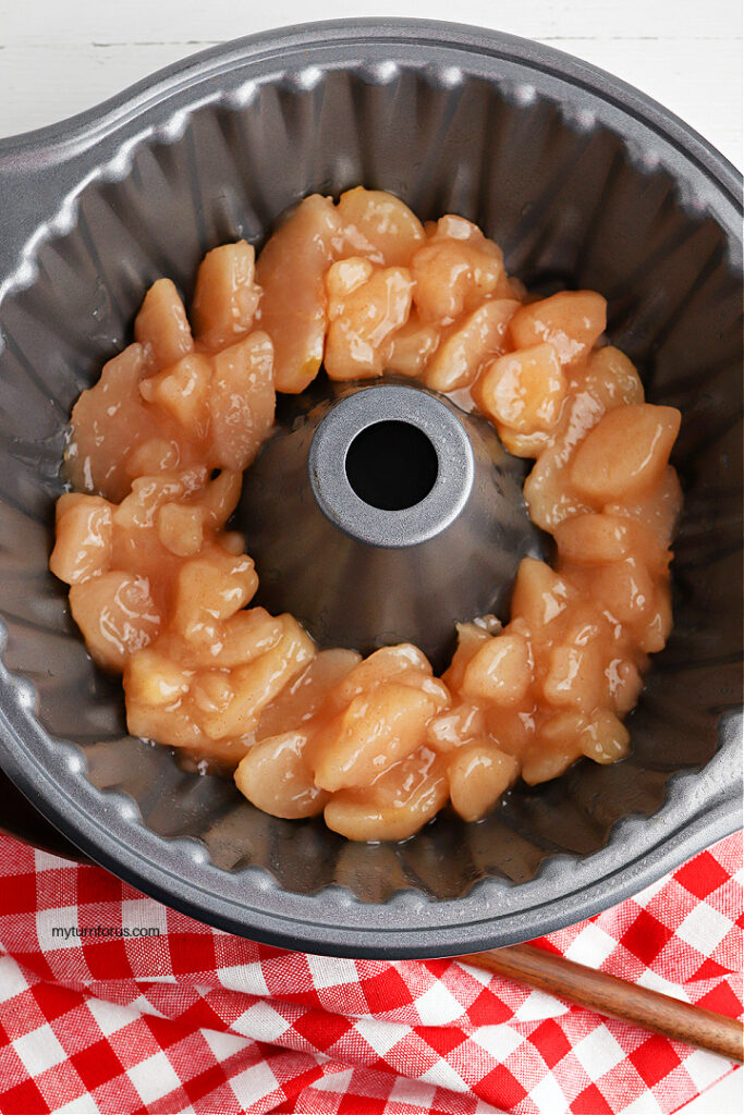 Apple pie filling spread in the bottom of a greased Bundt pan for caramel apple cake.