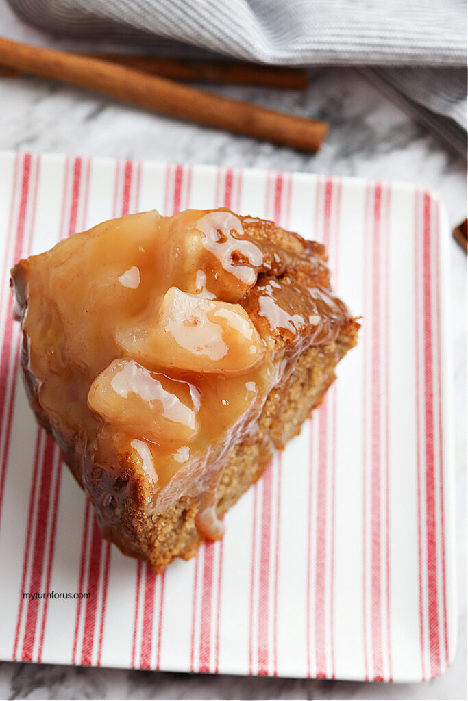 Slice of caramel apple Bundt cake with apple topping and caramel sauce on a striped plate.