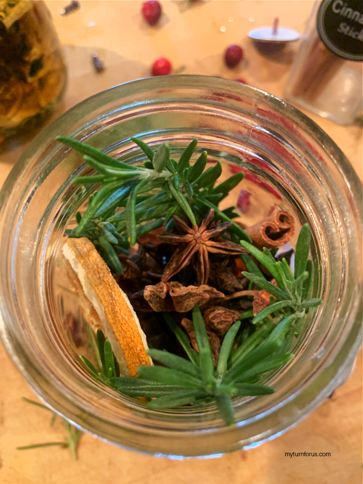 Adding Rosemary to the pinecones, orange slices and cinnamon sticks in a mason jar