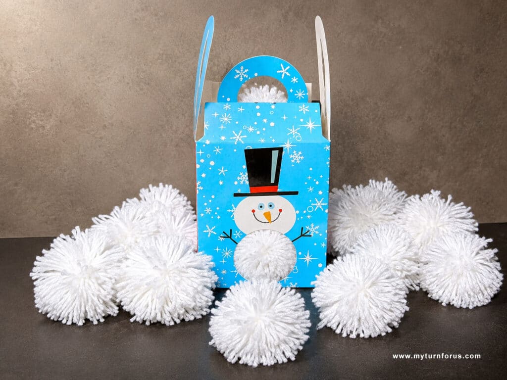 indoor snowball game, pom pom maker DIY yarn pom pom balls displayed in front of a blue winter snowman box.