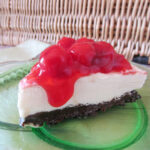 Vanilla ice cream pie slice topped with cherry pie filling and served on a green glass plate.