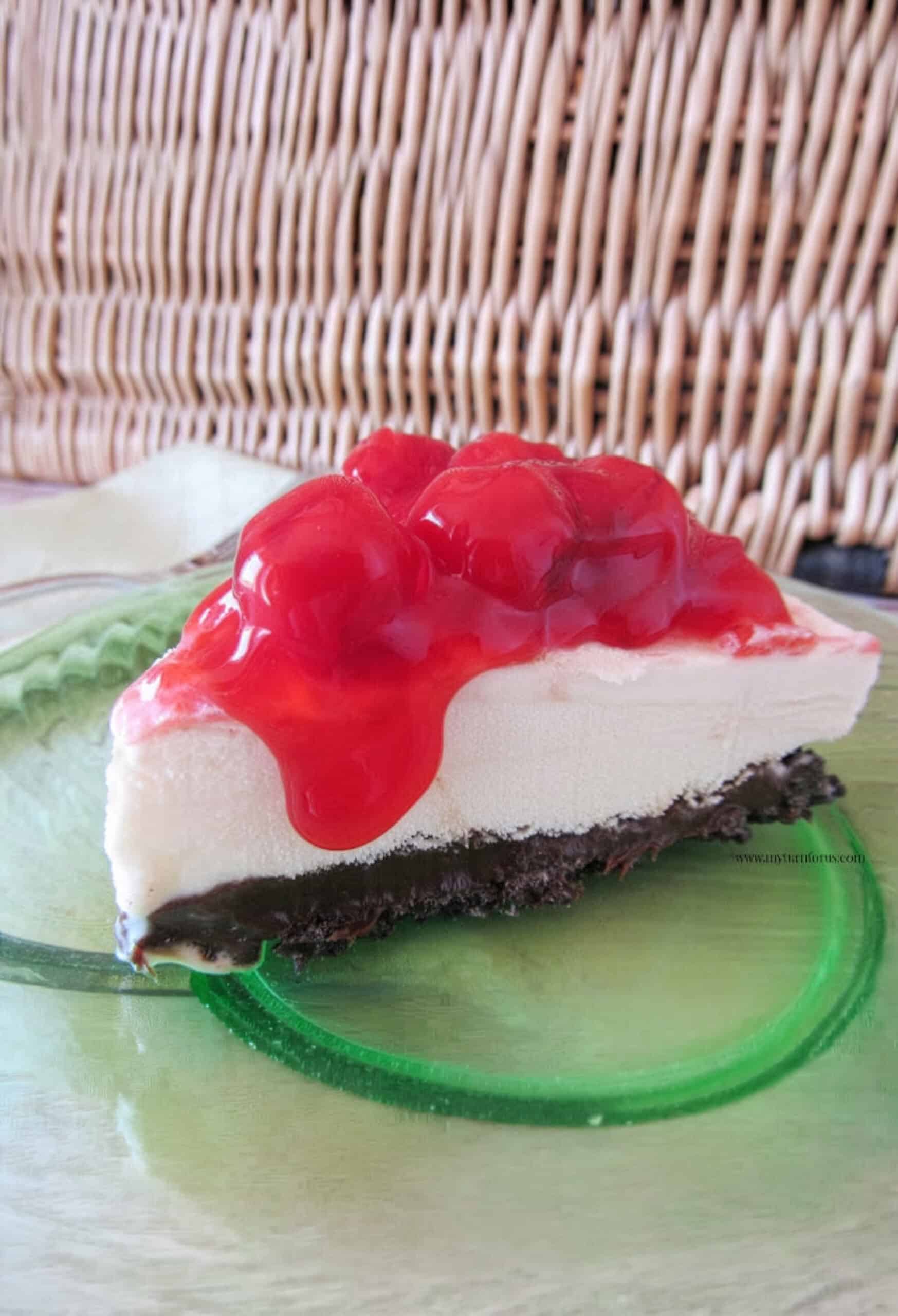 Vanilla ice cream pie slice topped with cherry pie filling and served on a green glass plate.